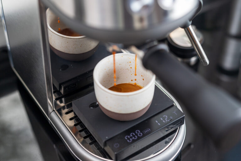 The shiny backsplash is angled, and reflects the cup and drip tray area on an angle.