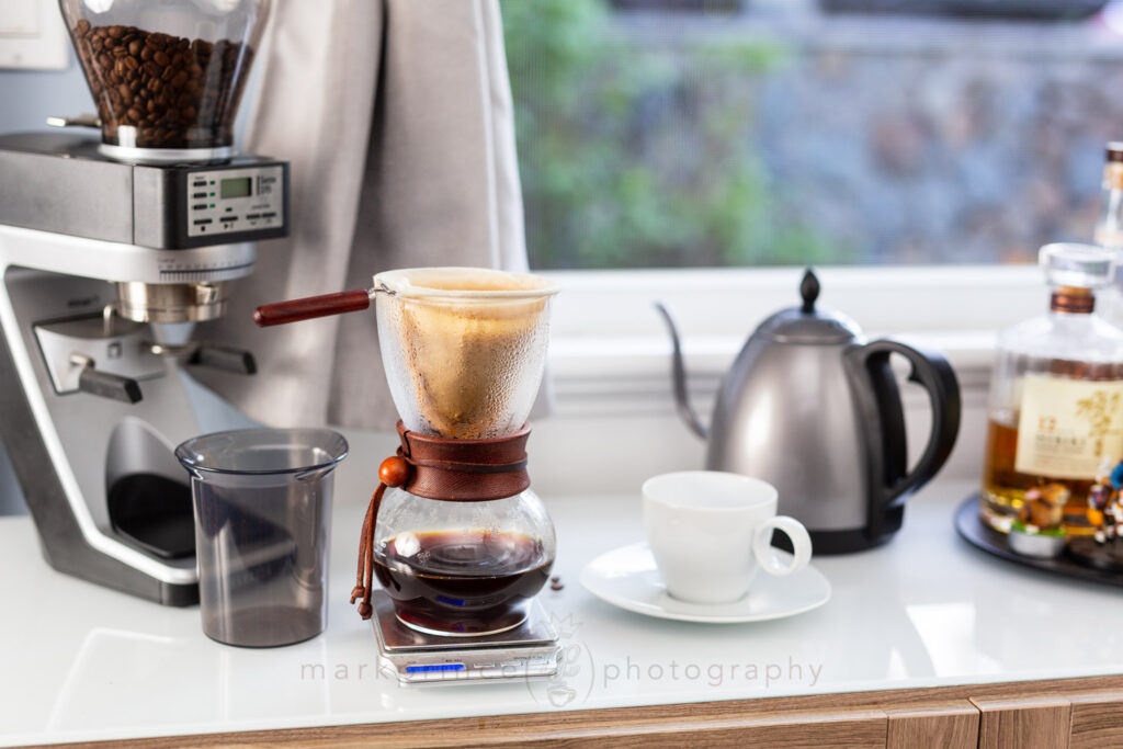 Brewing coffee with a cloth pour over device, with grinder and kettle in the background.