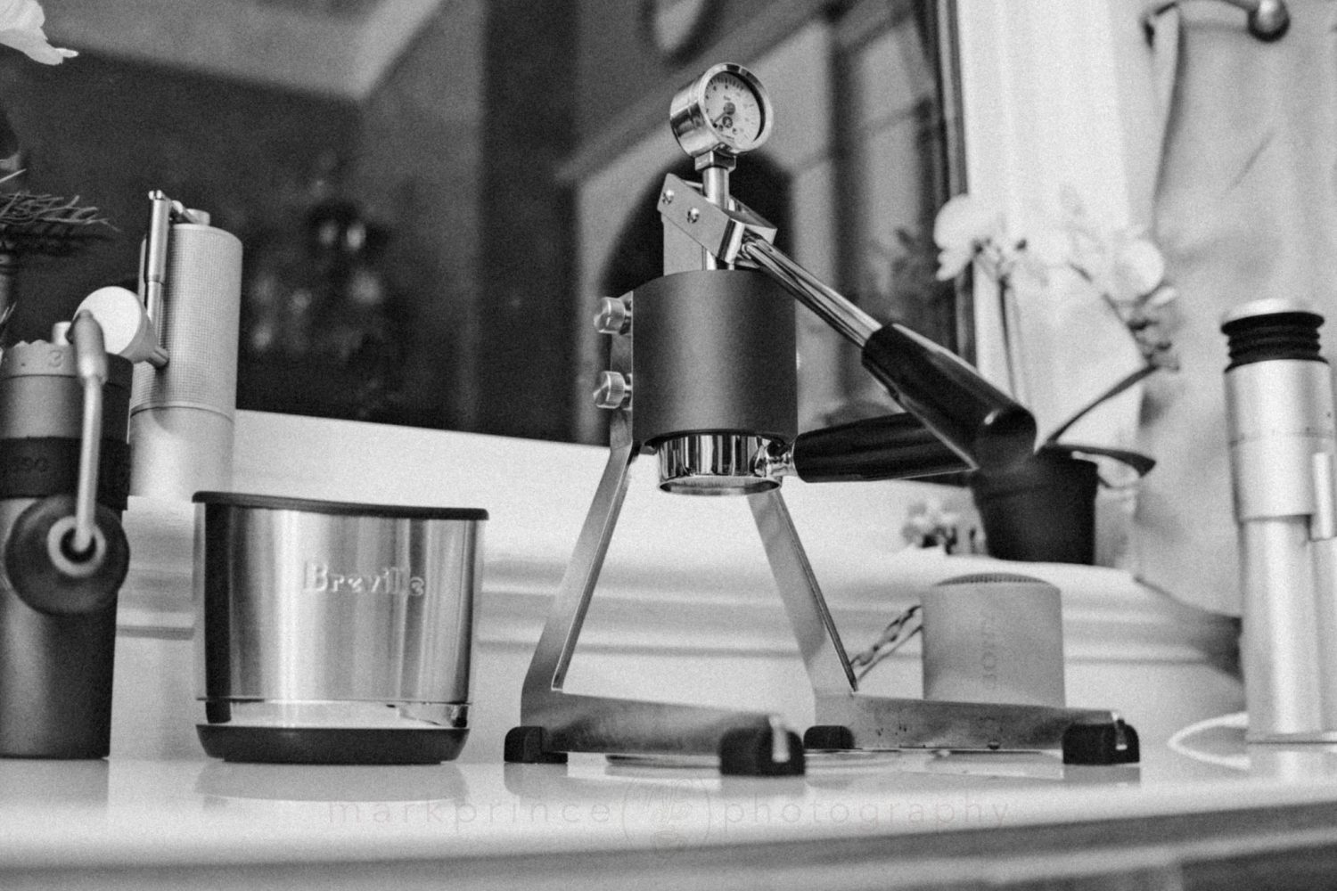 The Olympia Mina Lever Machine on a counter with hand grinders and a knockbox.