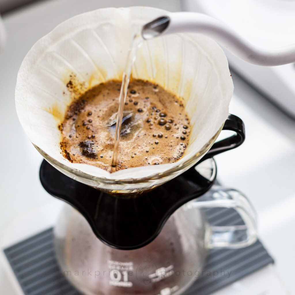 Pouring water into the bed of coffee in a Hario V60 coffee brewer.