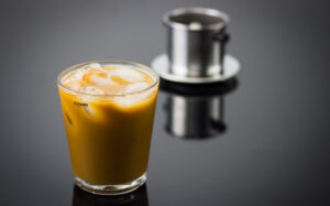 A finished brew of Vietnamese styled icded coffee, with the brewer in the background.